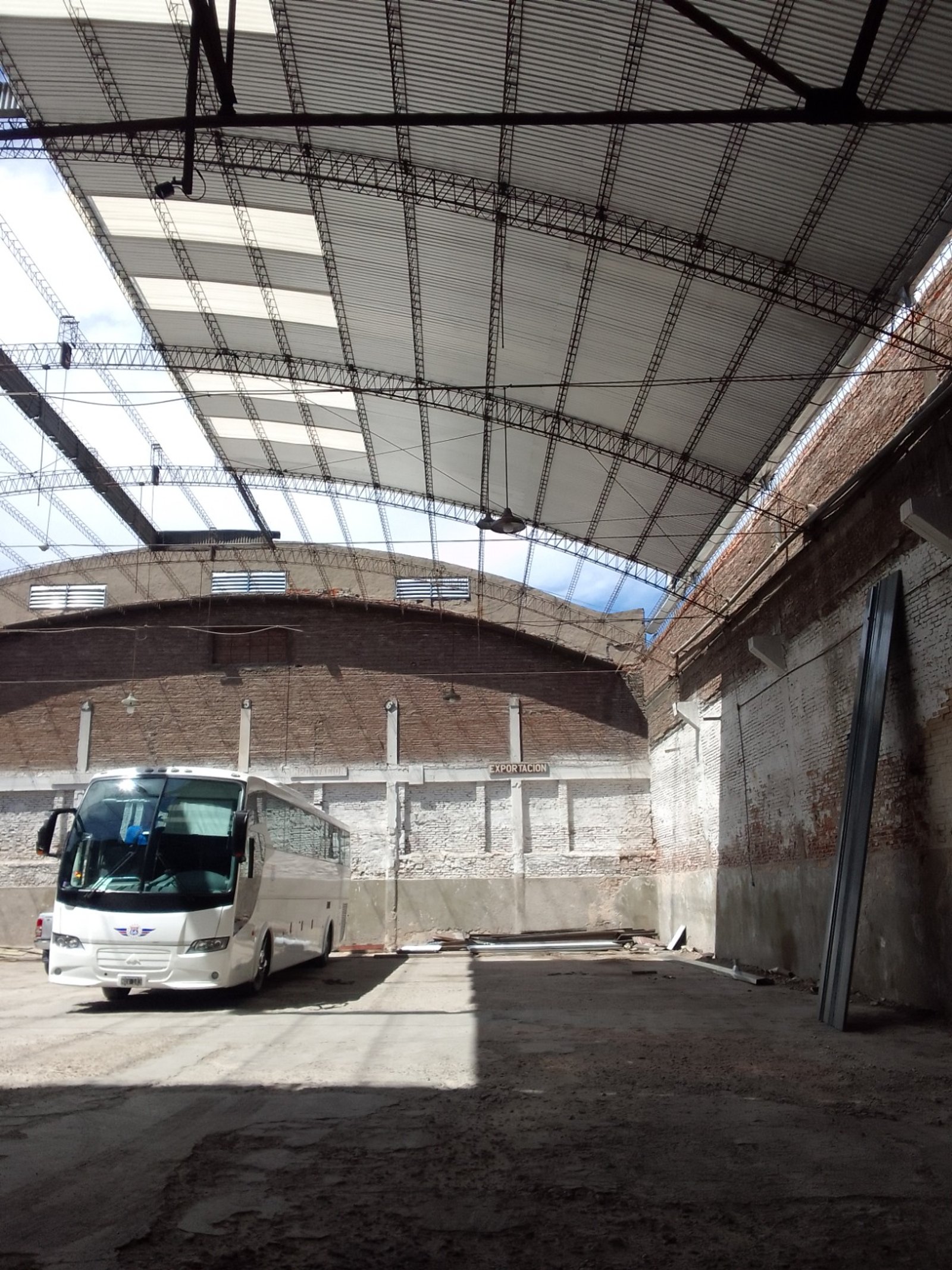 Interior de nave industrial con techo metálico y bus blanco — proyecto Galpon en Avellaneda, por Arquitecto Guido Niccoli, en Avellaneda
